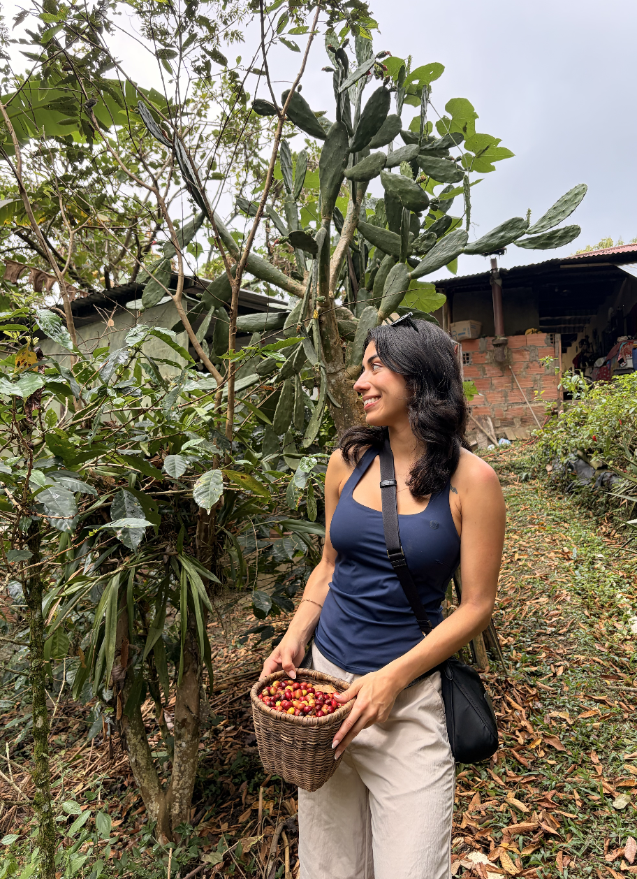 Jasmin smiling beside a cactus, holding a basket of coffee cherries